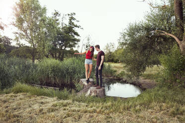 Mann hilft Frau beim Balancieren auf Baumstämmen im Teich, Wilhelminenberg, Wien, Österreich - CUF53827