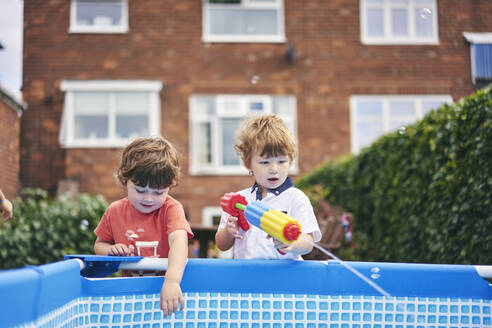 Jungen spielen mit Wasserpistole am Pool - CUF53838