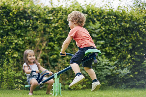 Girl and boy on toy seesaw in garden - CUF53842