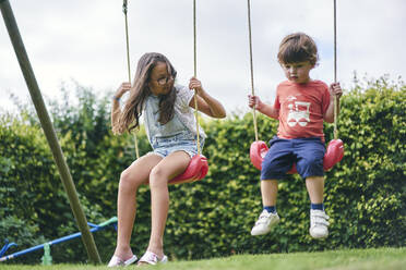 Sister and younger brother on swings in garden - CUF53844