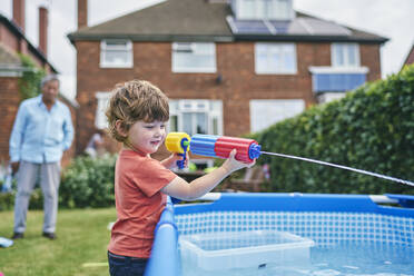 Junge spielt mit Wasserpistole am Pool - CUF53851