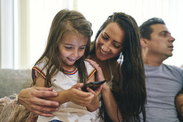 Mother watching daughter play computer game, father in background - CUF53858