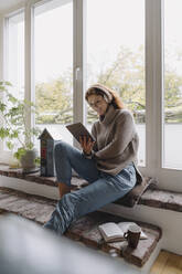 Mature woman sitting on wondow sill, using digital tablet - JOSF04052