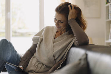 Lächelnde Frau, die auf der Couch sitzt und ein digitales Tablet benutzt - JOSF04055