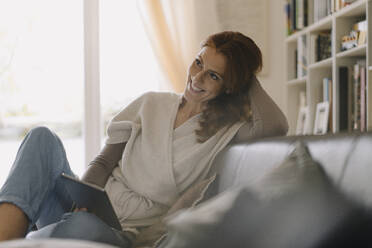 Smiling woman sitting on couch, using digital tablet - JOSF04056