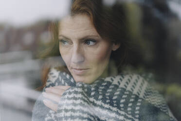 Woman looking out of window, wrapped in blanket - JOSF04066