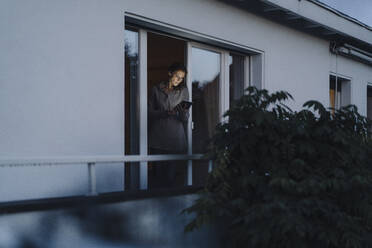 Frau steht in der Balkontür und benutzt ein digitales Tablet - JOSF04081