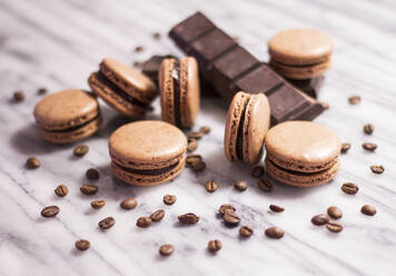 Close-up of macaroons with chocolate bar and coffee beans on table - CAVF70596