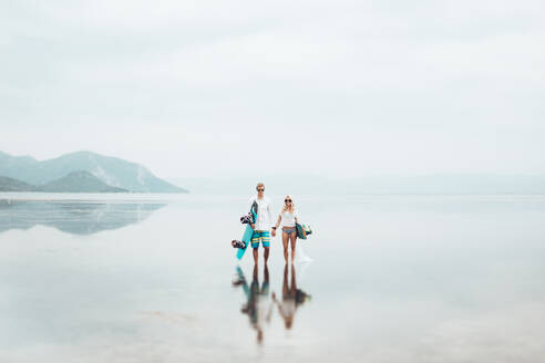 Couple with surfboard standing in sea against sky during foggy weather - CAVF70739