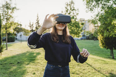 Young woman looking through VR headset in park - CUF53906