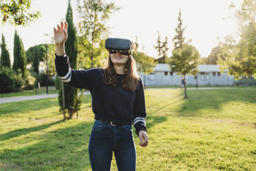 Young woman looking through VR headset in park - CUF53908