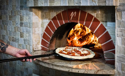 Koch schiebt Pizza in den Steinofen - CUF53919