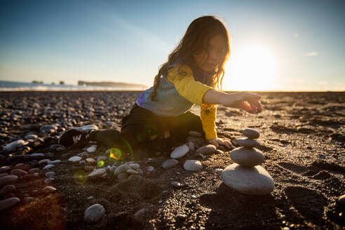 Kleines Mädchen stapelt Wunschsteine, schwarzer Sandstrand, Reynisfjara, Island - CUF53949
