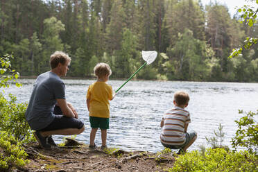 Vater und Söhne spielen mit Fischernetz am See, Finnland - CUF53974