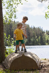 Brothers playing on upside down boat near lake, Finland - CUF53983
