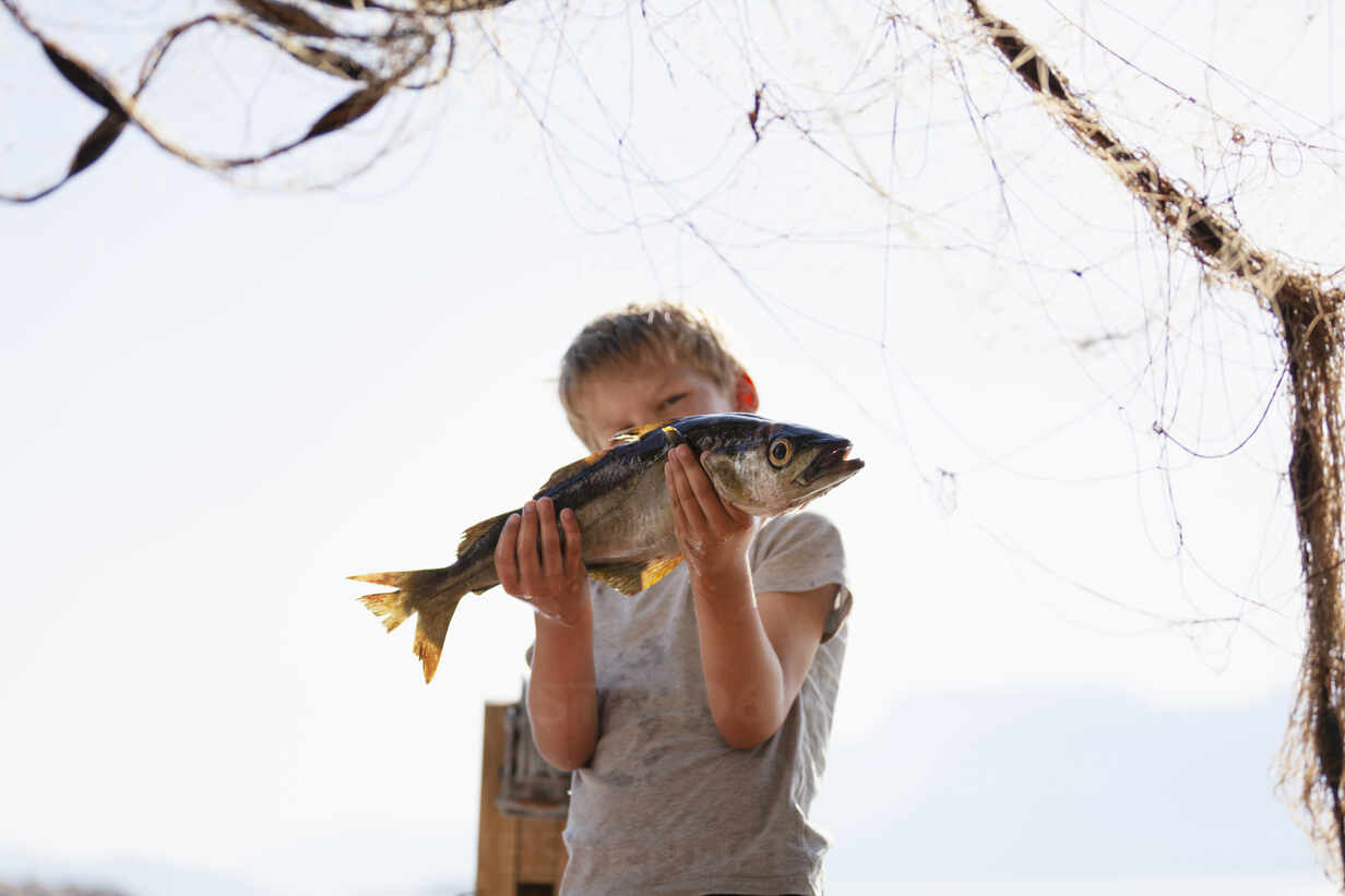 Boy holding up fish, fishing net in foreground stock photo