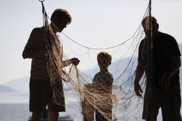 Fischer und Junge beim Entwirren des Fischernetzes - CUF53991
