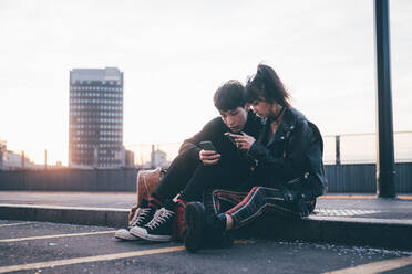 Junges Paar schreibt eine SMS auf dem Bordstein, Mailand, Italien - CUF54105