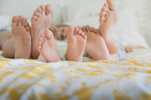 Three pairs of bare feet in a row, different sizes on a bed - CUF54139