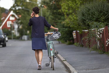 Woman pushing bike along road - JOHF04863