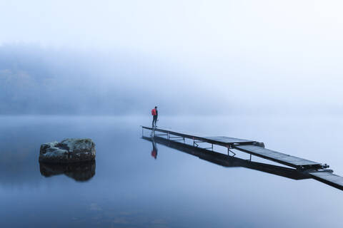 Mann auf Pier im See im Morgennebel, lizenzfreies Stockfoto