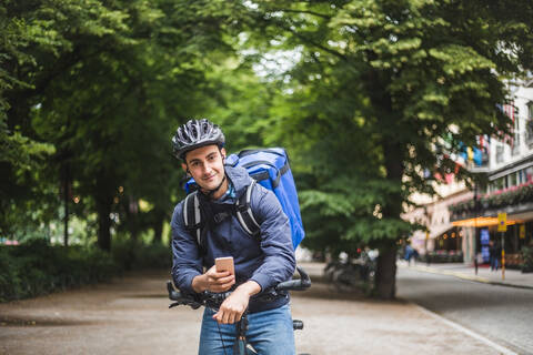 Porträt eines selbstbewussten Lebensmittellieferanten mit Fahrrad in der Stadt, lizenzfreies Stockfoto