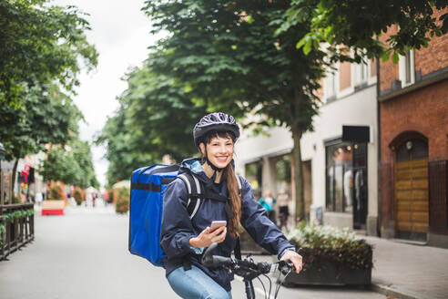 Portrait of smiling food delivery woman with bicycle on city street - MASF15283