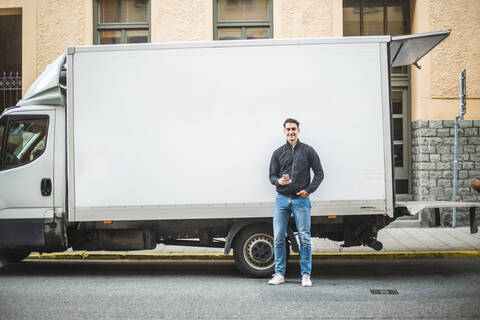 Porträt eines männlichen Möbelpackers, der auf einer Straße in der Stadt vor einem Lastwagen steht, lizenzfreies Stockfoto