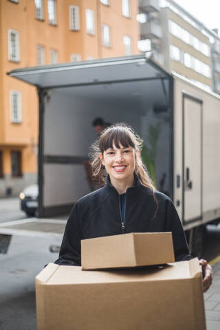 Porträt eines lächelnden weiblichen Möbelpackers, der Kartons trägt, lizenzfreies Stockfoto