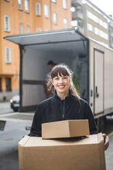 Portrait of smiling female mover carrying cardboard boxes - MASF15313