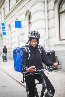 Lebensmittellieferantin mit Smartphone auf der Straße in der Stadt - MASF15320