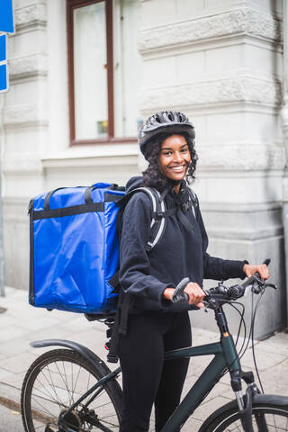 Porträt einer lächelnden Zustellerin mit Fahrrad in der Stadt, lizenzfreies Stockfoto