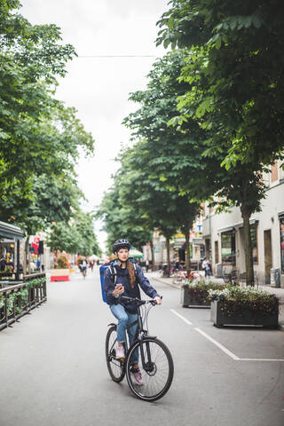 Lebensmittellieferantin mit Fahrrad auf der Straße in der Stadt, lizenzfreies Stockfoto