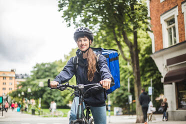 Lächelnde Lebensmittellieferantin mit Fahrrad auf der Straße in der Stadt - MASF15337
