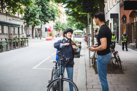 Auslieferungsfrau im Gespräch mit einem männlichen Kunden auf dem Bürgersteig in der Stadt, lizenzfreies Stockfoto