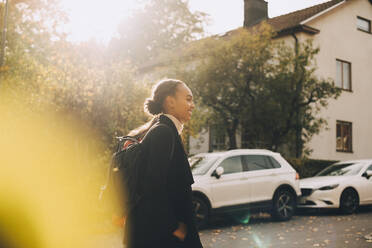 Seitenansicht von Teenager-Mädchen zu Fuß gegen Autos und Haus im Herbst - MASF15375