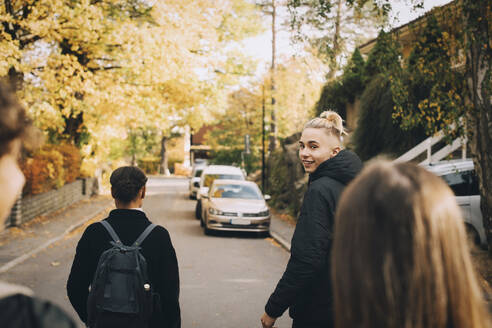 Porträt eines lächelnden Teenagers, der mit Freunden auf einer Straße in der Stadt spazieren geht - MASF15382