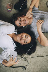 Direkt über der Aufnahme eines Teenagers, der ein Selfie mit seiner Freundin macht, während sie zusammen auf dem Teppich zu Hause liegen - MASF15392