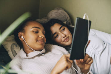 Female teenagers listening music on digital tablet while lying on bed at home - MASF15406
