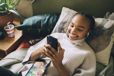 Hohe Winkel Ansicht der lächelnden Teenager-Mädchen Musik hören, während mit Handy auf dem Bett zu Hause - MASF15413