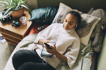 Hohe Winkel Ansicht der weiblichen Teenager Musik hören, während mit Smartphone auf dem Bett zu Hause - MASF15414