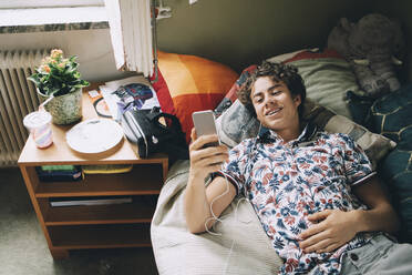 Hohe Winkel Ansicht der lächelnden Teenager hören Musik durch Handy auf dem Bett zu Hause - MASF15416