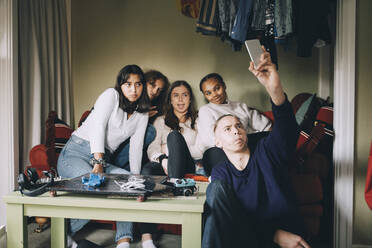 Freunde machen ein Selfie mit ihrem Smartphone und schneiden dabei Grimassen im heimischen Wohnzimmer - MASF15421