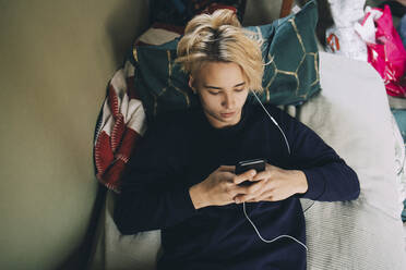 Hohe Winkel Ansicht der männlichen Teenager Text-Messaging auf dem Handy, während im Schlafzimmer liegen - MASF15428