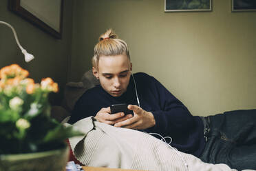 Männlicher Teenager, der ein Smartphone benutzt, während er sich zu Hause auf dem Bett ausruht - MASF15429