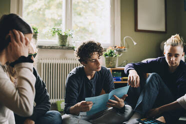 Jugendlicher liest Broschüre, während er mit Freunden im Schlafzimmer sitzt - MASF15439