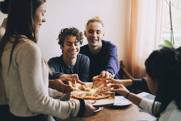 Teenager-Mädchen serviert Pizza an glückliche Freunde am Esstisch - MASF15453