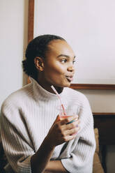 Smiling teenage girl looking away while having smoothie at home - MASF15465