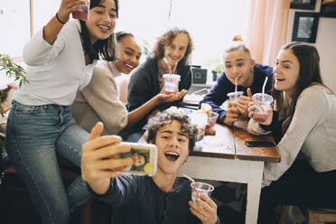 Jugendlicher, der ein Selfie mit Freunden auf seinem Smartphone macht, während er zu Hause einen Smoothie trinkt - MASF15466