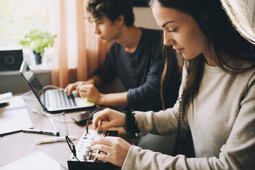 Teenager-Mädchen beim Einstellen eines Tonmischers, während sie mit einem Freund zu Hause am Laptop sitzt - MASF15475